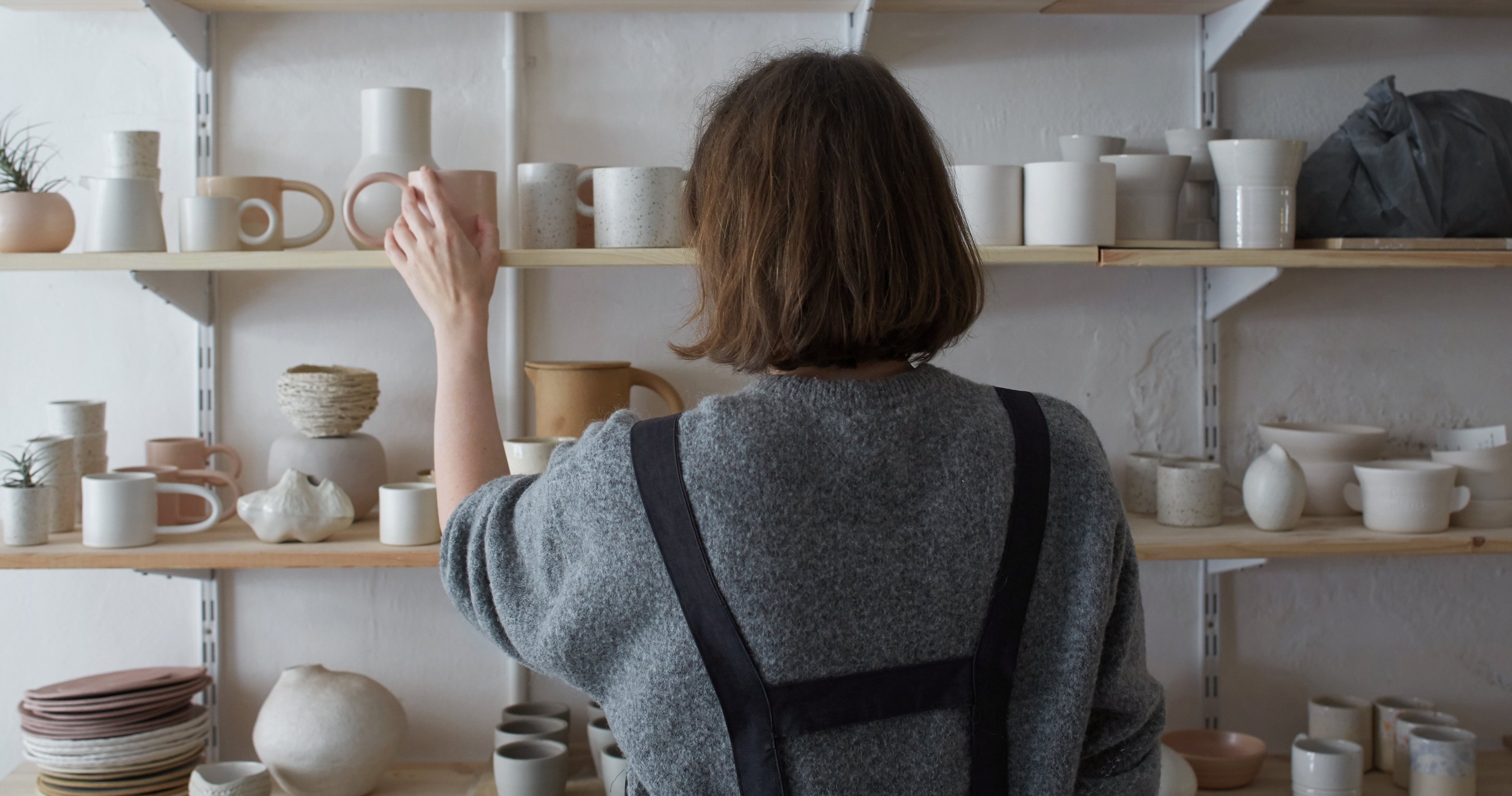 Rear view of a ceramic shop owner organizing her stock room.